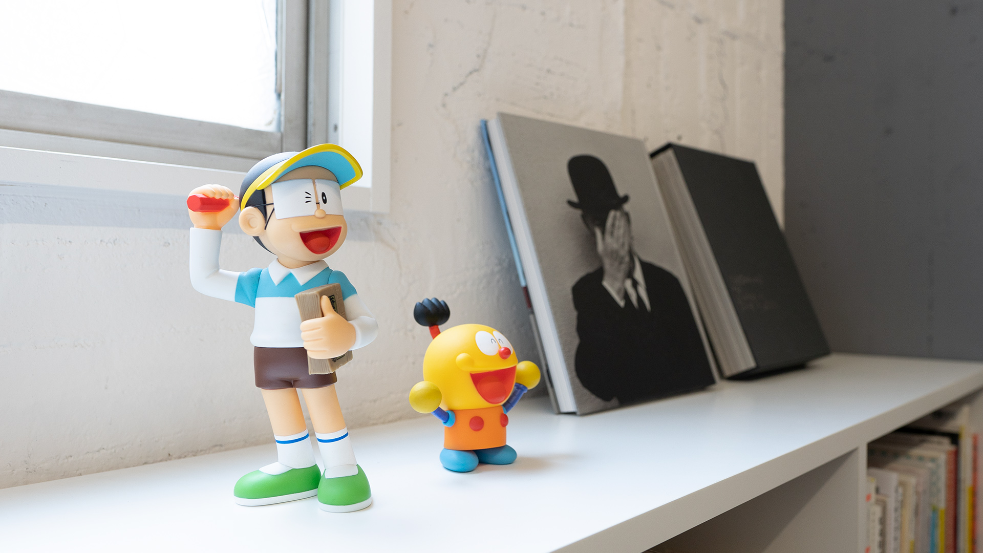 オフィスの本棚にディスプレイされているキテレツとコロ助のフィギュアと、マグリットとエディ・スリマンの写真集